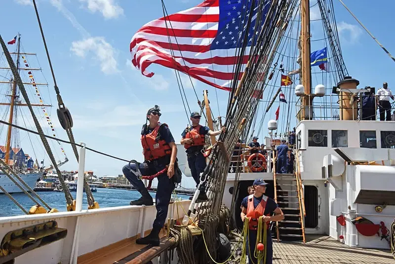 斯蒂森站在一艘大船的边缘，一面美国国旗在她头上飘扬，她旁边站着两名船员